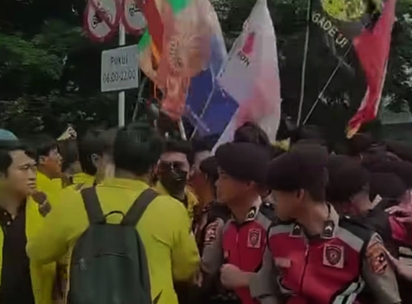 Crowd of people at an outdoor demonstration, holding colorful flags and banners with uniforms visible in the front.