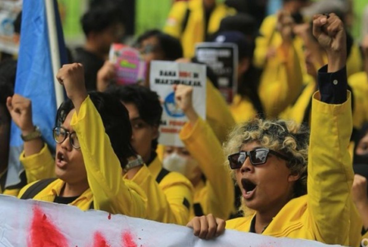 Protesters in yellow jackets raise fists, shouting slogans at a rally, holding signs and banners