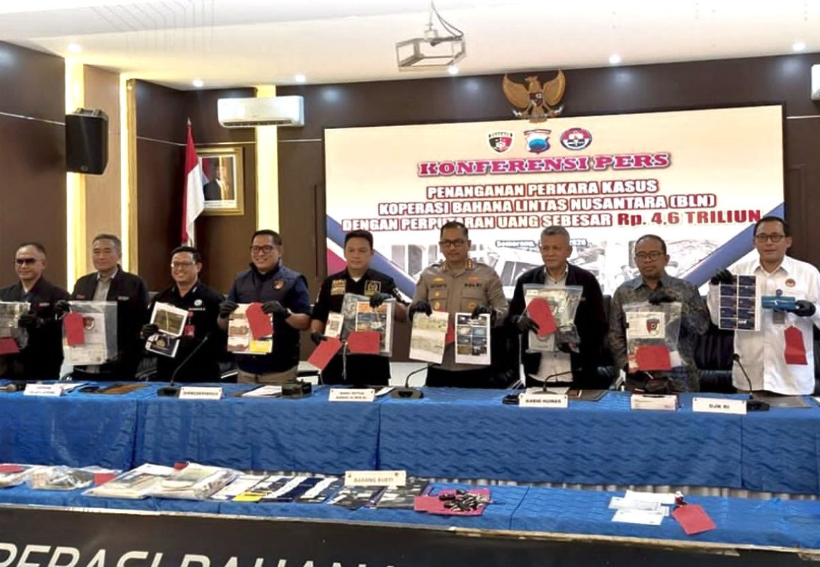 Indonesian officials stand behind a blue-draped table, displaying seized documents and evidence at a press conference with a large banner in the background.