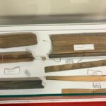 Display case containing bundled parchment scrolls tied with string and several wooden rulers with labels, as a museum exhibit item.