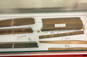 Display case containing bundled parchment scrolls tied with string and several wooden rulers with labels, as a museum exhibit item.