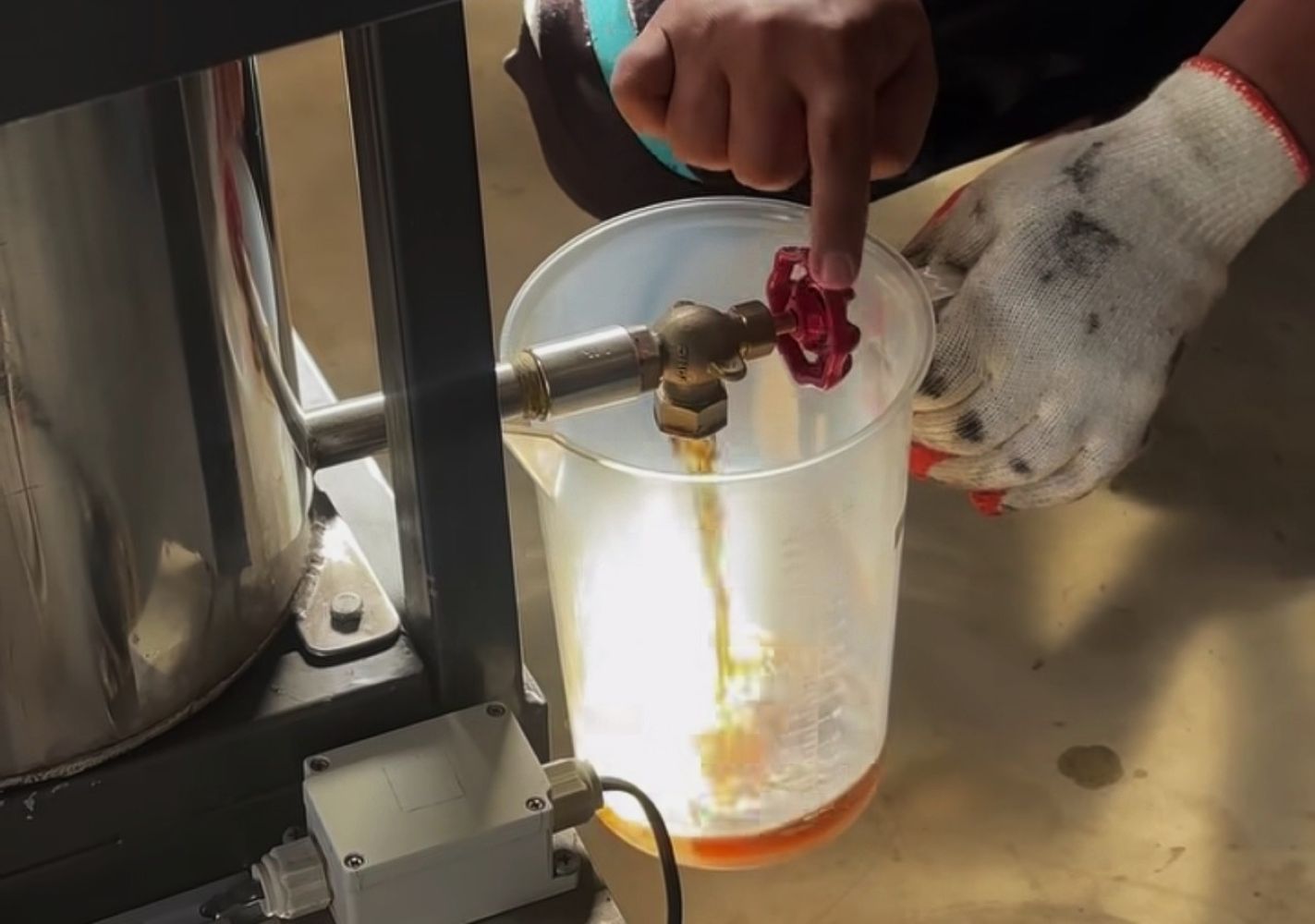 Person wearing gloves turns a red valve to release liquid into a translucent beaker on a lab bench area.