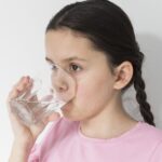 Girl wearing a pink shirt drinking water from a clear glass.