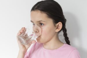 Girl wearing a pink shirt drinking water from a clear glass.