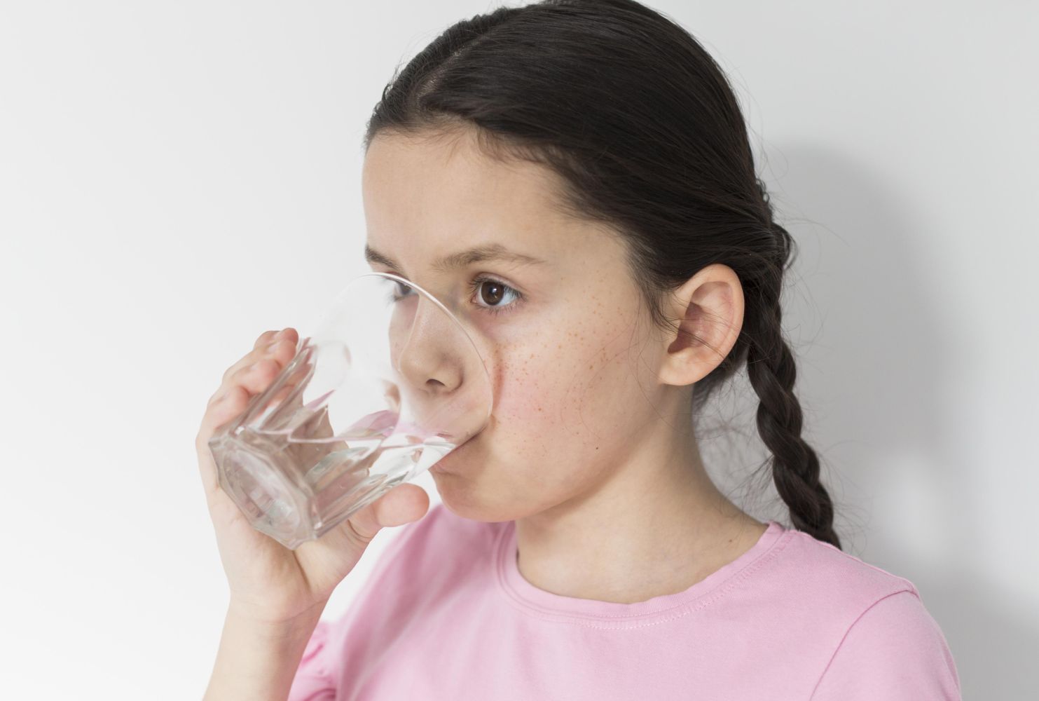 Girl wearing a pink shirt drinking water from a clear glass.