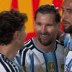 Two soccer players in Argentina national team jerseys celebrate together on the field, smiles visible amid a group celebration.