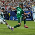 Soccer players from Argentina (blue-and-white stripes) and a green-clad opponent contest the ball on a crowded field during a match.