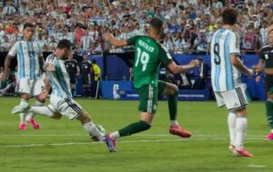 Soccer players from Argentina (blue-and-white stripes) and a green-clad opponent contest the ball on a crowded field during a match.