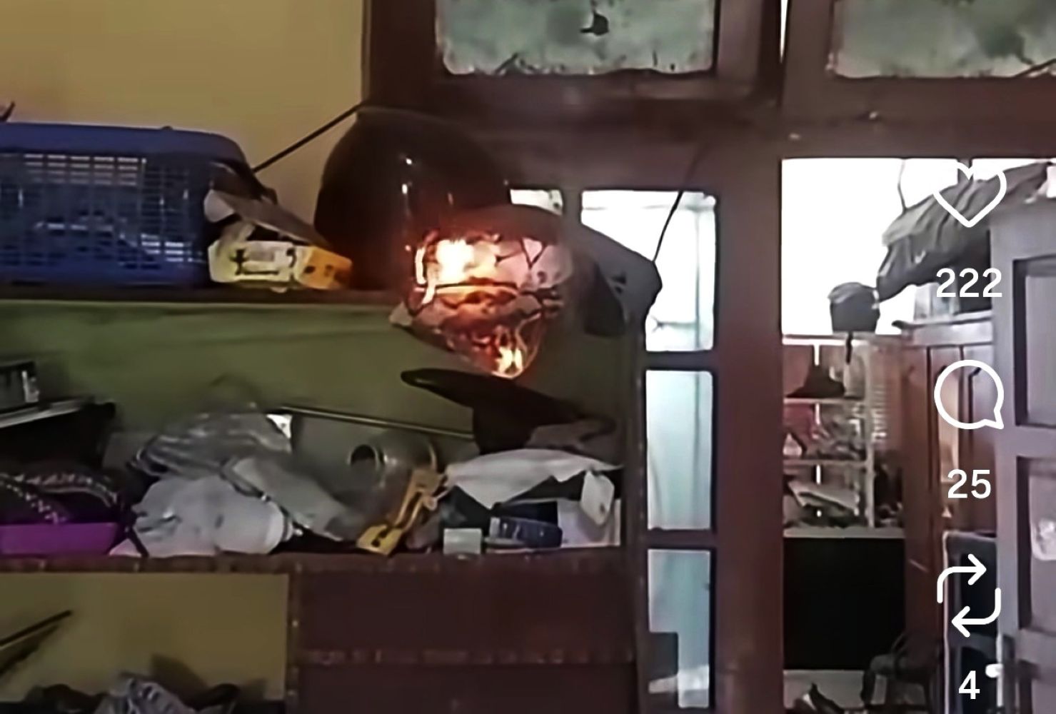 Helmet on a cluttered shelf is burning, with visible flames and smoke in a dim room.