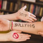 Forearm with 'STOP BULLYING' written in black, surrounded by open hands in a supportive pose.