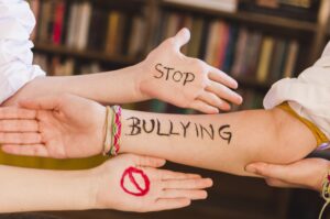 Forearm with 'STOP BULLYING' written in black, surrounded by open hands in a supportive pose.
