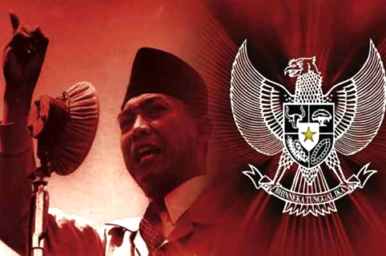 Man in a traditional cap speaks into a microphone, with the Indonesian Garuda emblem in the red background behind him.