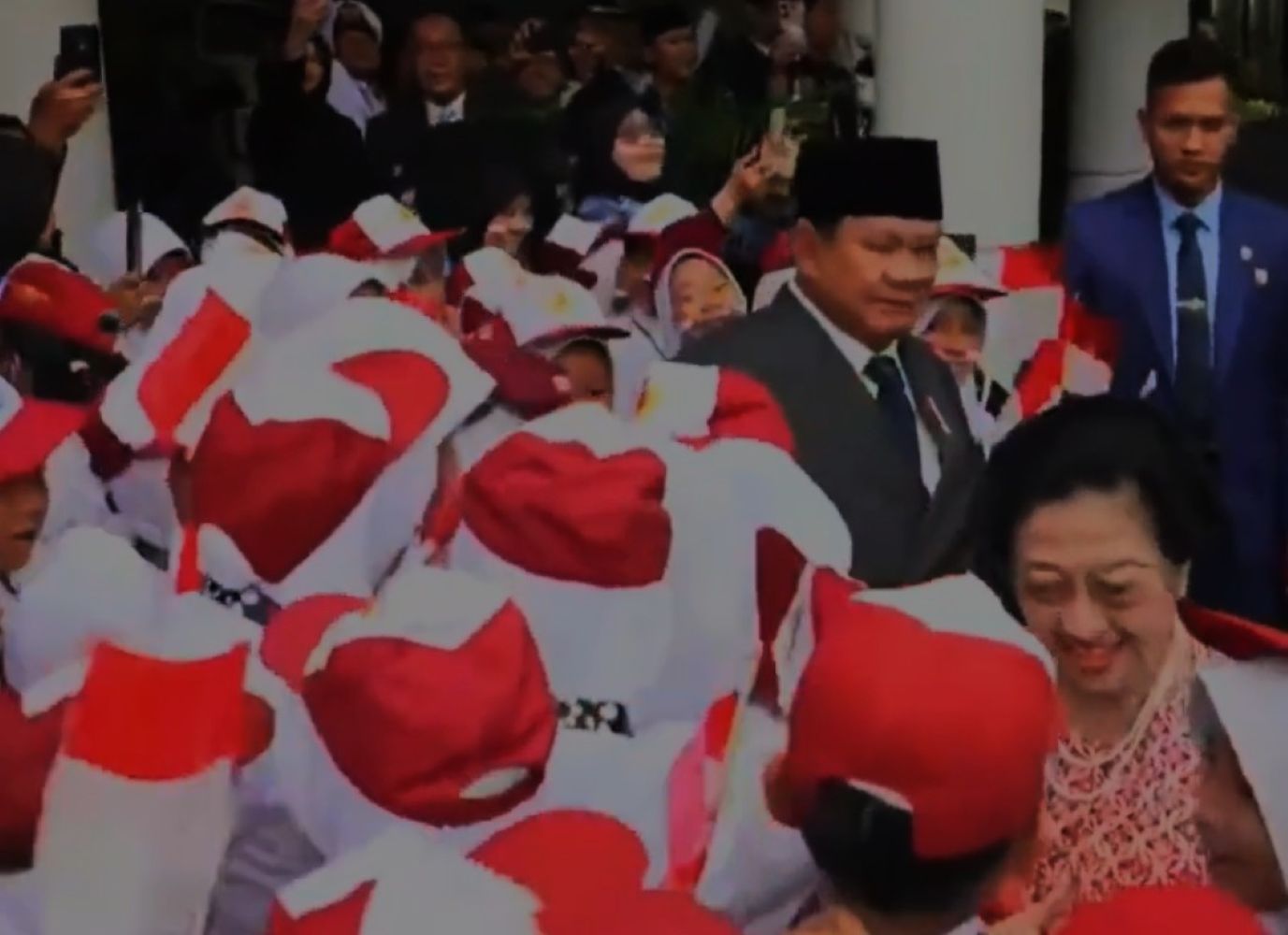 Crowd of people in red-and-white outfits waving Indonesian flags at a public ceremony; a smiling woman stands in the foreground.
