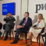 Panel of four professionals seated on stage in a discussion, PwC logo visible behind them and a blue screen reading 'Navigating Global Shifts' on the left.