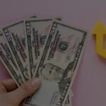 Fanned stack of $50 bills held in a hand with a yellow upward arrow, symbolizing financial growth.