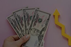 Fanned stack of $50 bills held in a hand with a yellow upward arrow, symbolizing financial growth.