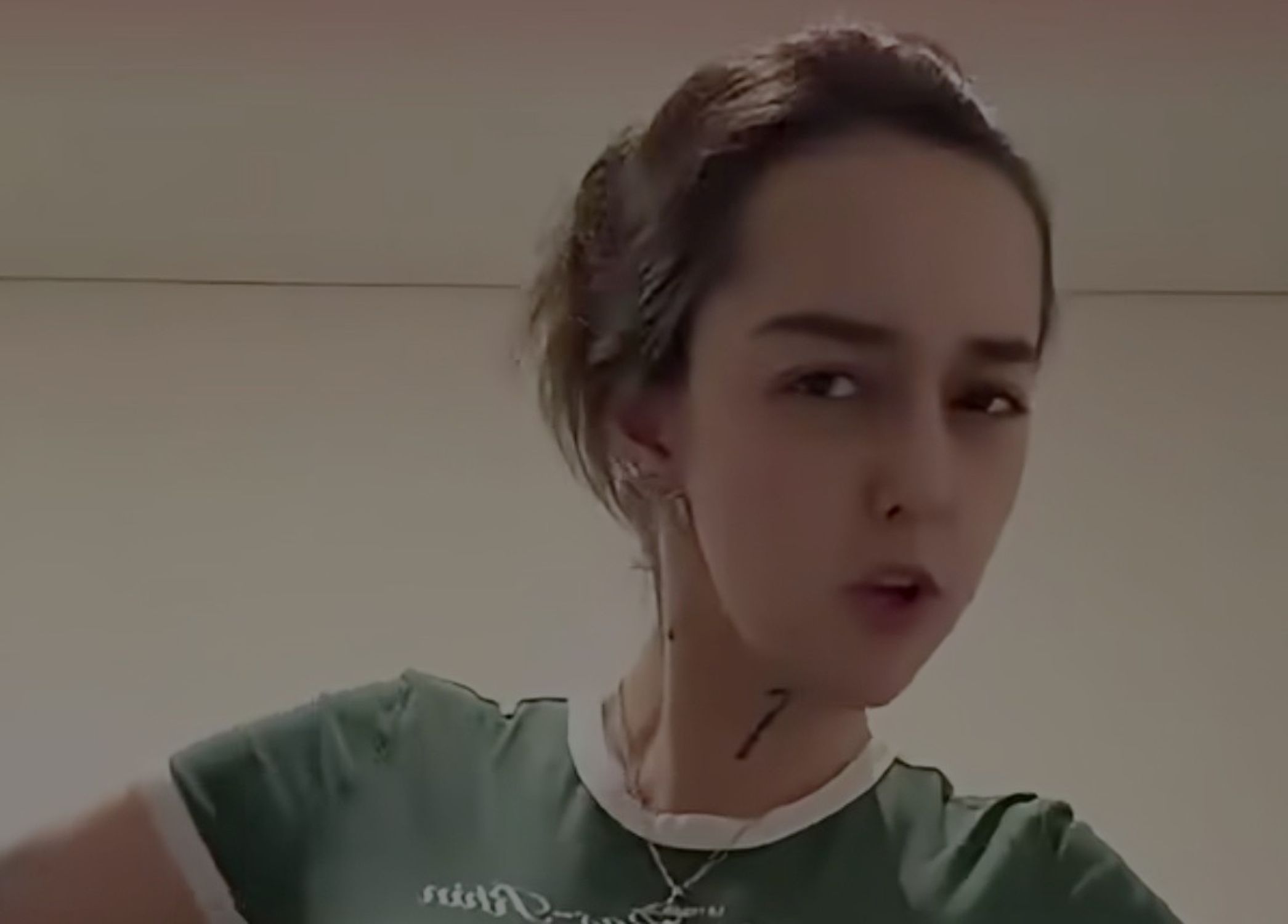 Close-up of a person wearing a green shirt with a white collar, looking at the camera indoors.