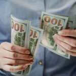 Person counting a fan of US $100 bills held in both hands