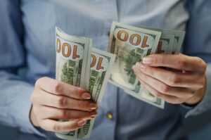 Person counting a fan of US $100 bills held in both hands