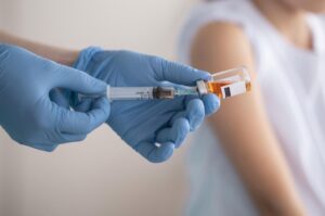 Medical worker in blue gloves draws vaccine from an amber vial into a syringe.