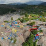 Aerial view of a rocky hillside turned into a makeshift camp with colorful tents and tarps scattered among the rocks.