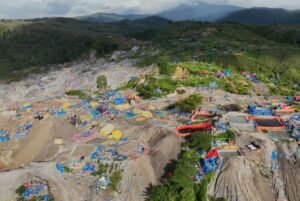 Aerial view of a rocky hillside turned into a makeshift camp with colorful tents and tarps scattered among the rocks.