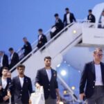 Group of men in dark blazers walking down stairs from a white airplane on the tarmac at the airport.