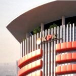 Modern office building with vertical columns and red curved accents, displaying the letters 'KPK' on the facade.