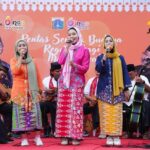 Group of four women in colorful traditional outfits singing on a stage with musicians behind them at a cultural event banner in Jakarta