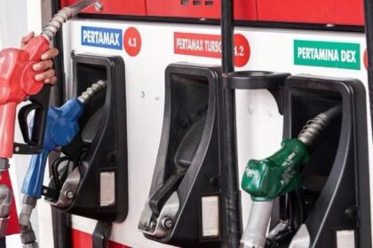 Gas pump panel with three nozzle handles (red, blue, green) at a fuel station, labeled Pertamax and Pertamina Dex.