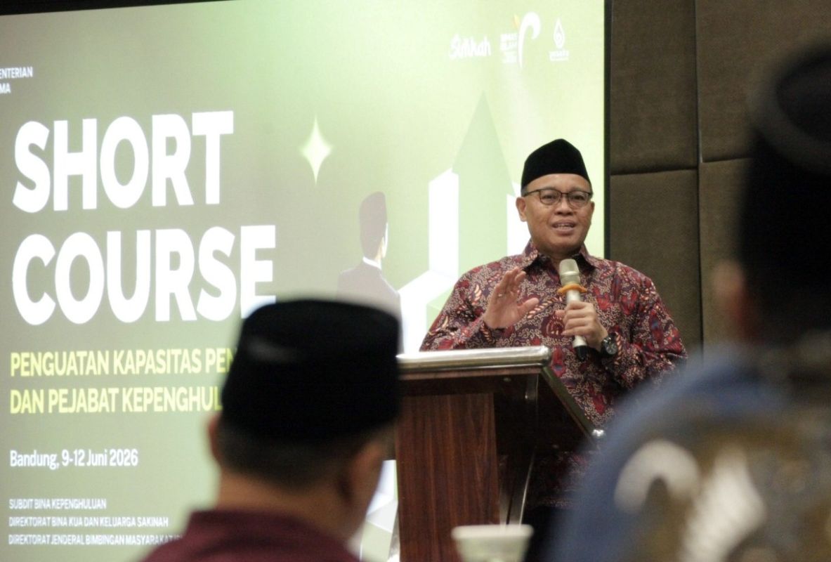 Man in batik shirt and black cap speaks at a podium during a seminar, with a large 'SHORT COURSE' banner behind.