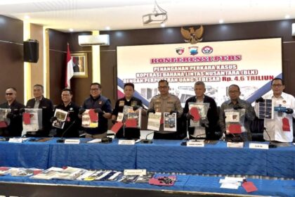 Indonesian officials stand behind a blue-draped table, displaying seized documents and evidence at a press conference with a large banner in the background.
