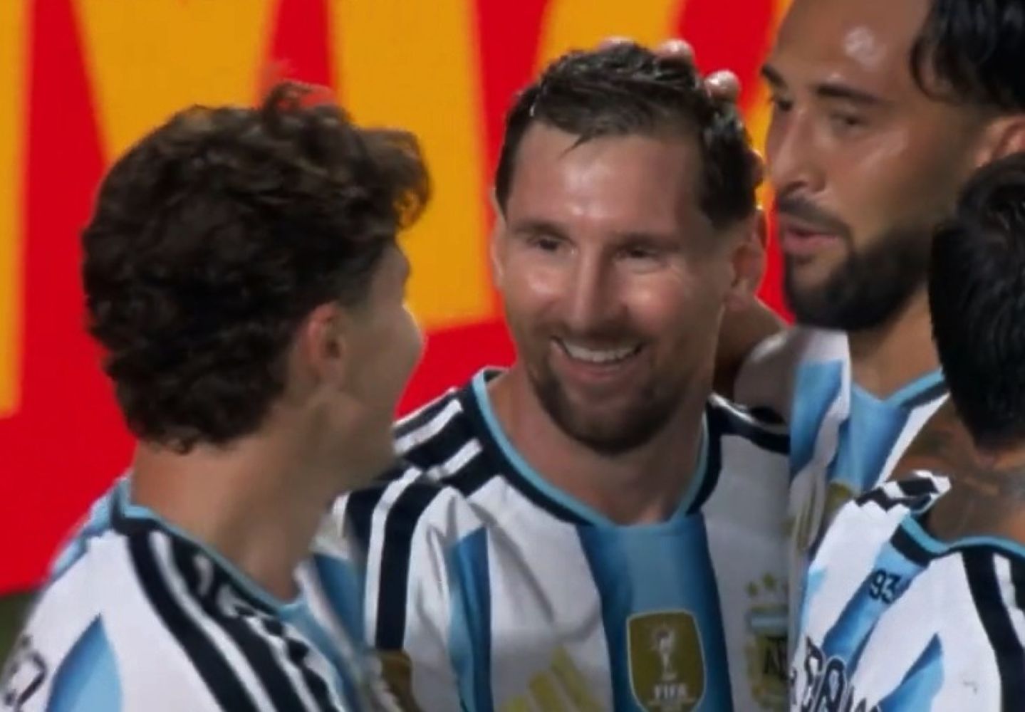 Two soccer players in Argentina national team jerseys celebrate together on the field, smiles visible amid a group celebration.