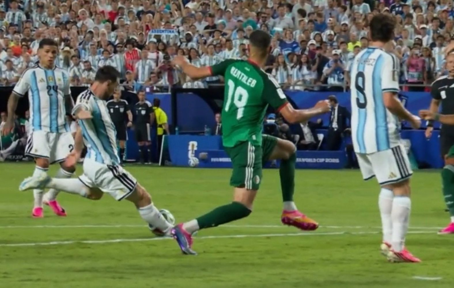 Soccer players from Argentina (blue-and-white stripes) and a green-clad opponent contest the ball on a crowded field during a match.