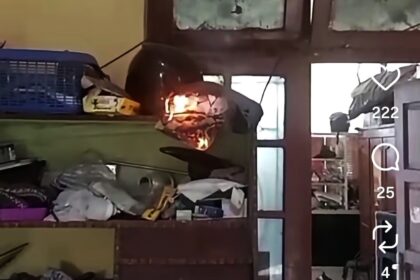 Helmet on a cluttered shelf is burning, with visible flames and smoke in a dim room.