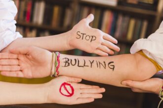 Forearm with 'STOP BULLYING' written in black, surrounded by open hands in a supportive pose.