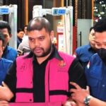 Man in a bright pink vest being escorted by two uniformed officers through a public area.