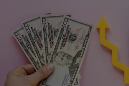 Fanned stack of $50 bills held in a hand with a yellow upward arrow, symbolizing financial growth.