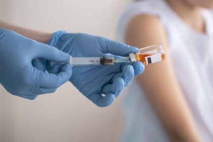 Medical worker in blue gloves draws vaccine from an amber vial into a syringe.