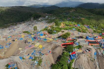 Aerial view of a rocky hillside turned into a makeshift camp with colorful tents and tarps scattered among the rocks.