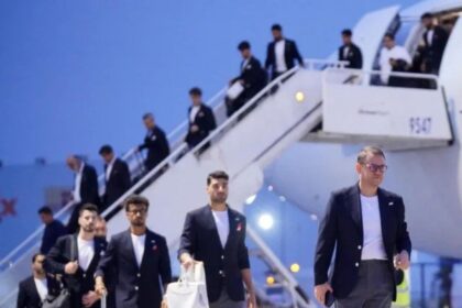 Group of men in dark blazers walking down stairs from a white airplane on the tarmac at the airport.