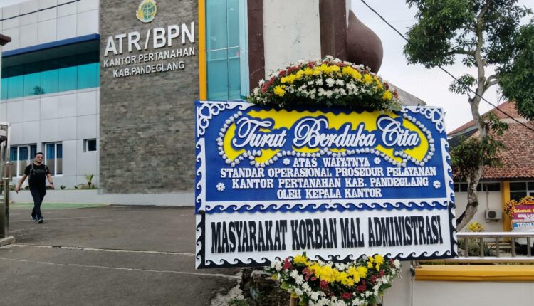 A government land office building (ATR/BPN) with a large blue condolence banner outside, featuring floral decorations and Indonesian text.