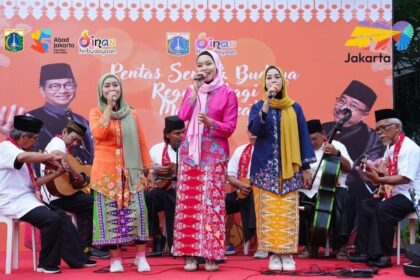 Group of four women in colorful traditional outfits singing on a stage with musicians behind them at a cultural event banner in Jakarta